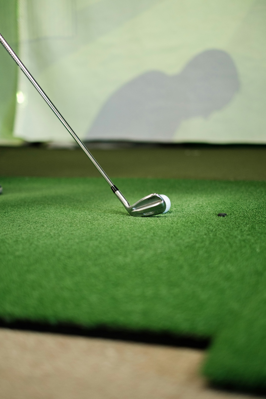 Golf club and ball on indoor turf in a simulator practice space
